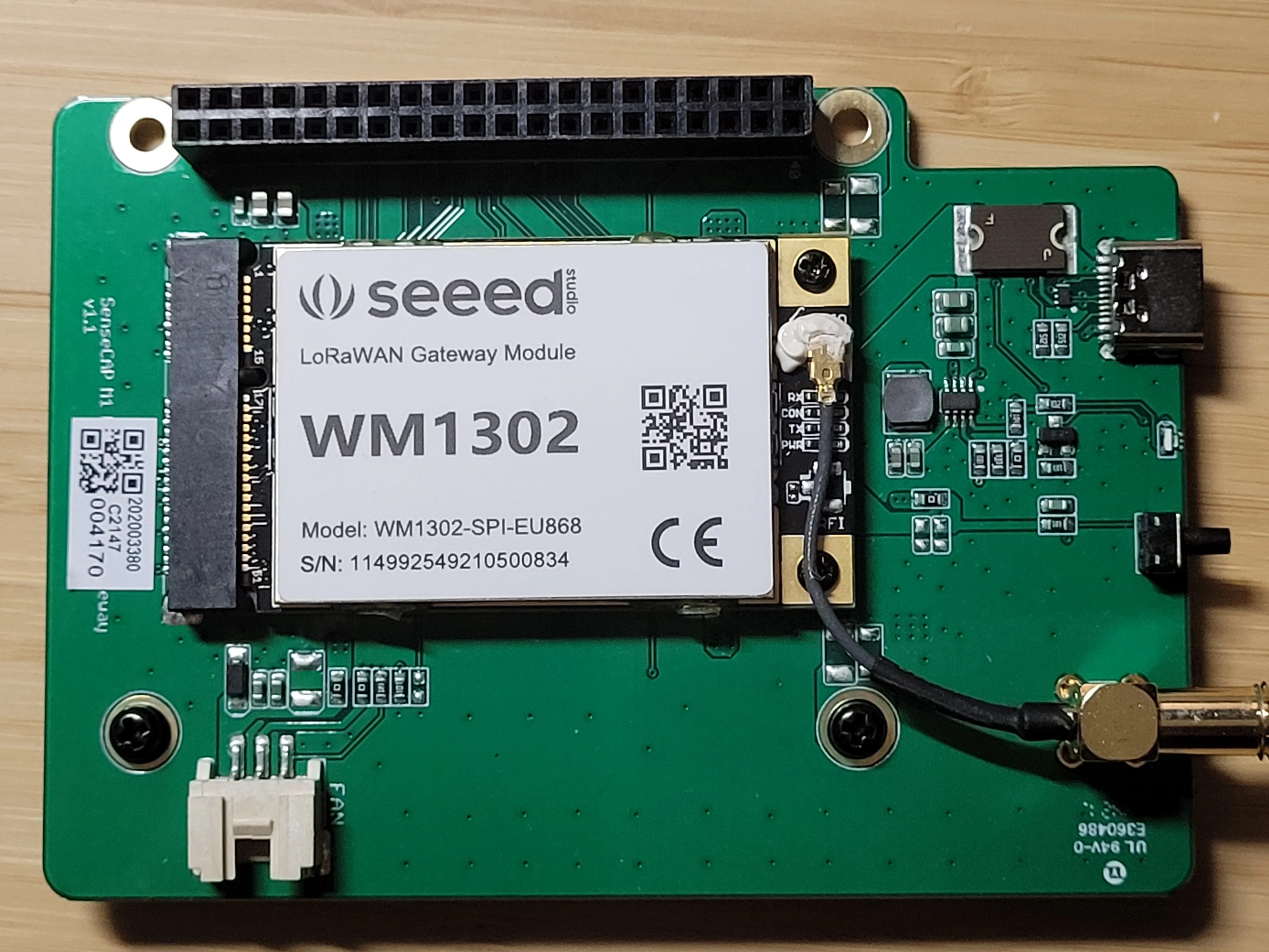 Green M1 carrier holding a labeled WM1302 SPI EU868 module beside USB-C, button, fan socket, and antenna cable